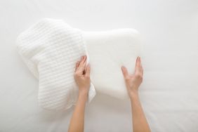Hands adjusting a white memory foam pillow with a removable cover