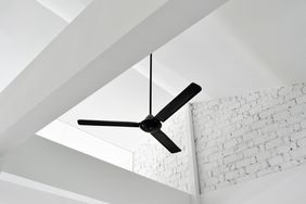 A ceiling fan installed on a white ceiling with exposed beams and brick wall background