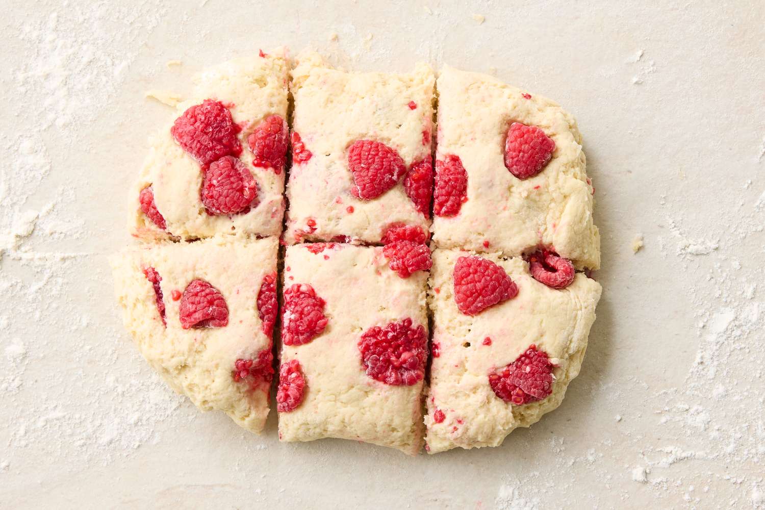 Six raspberry scone pieces dough cut into squares on a floured surface