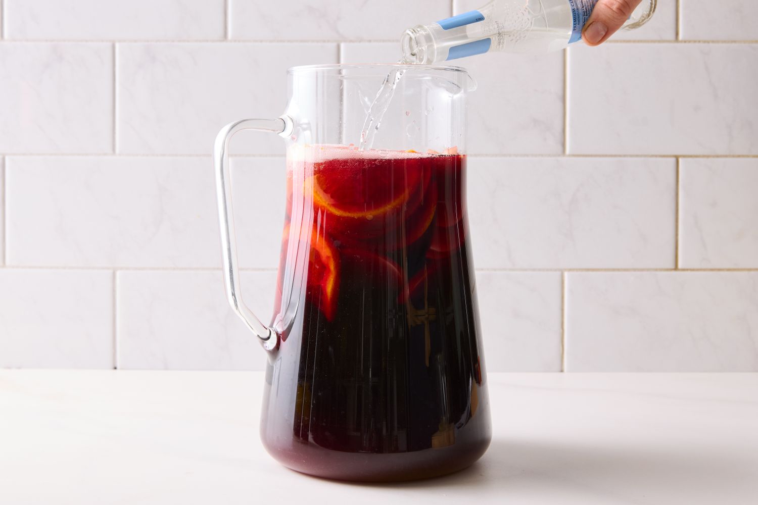 A pitcher of sangria being prepared with a sparkling liquid being poured in