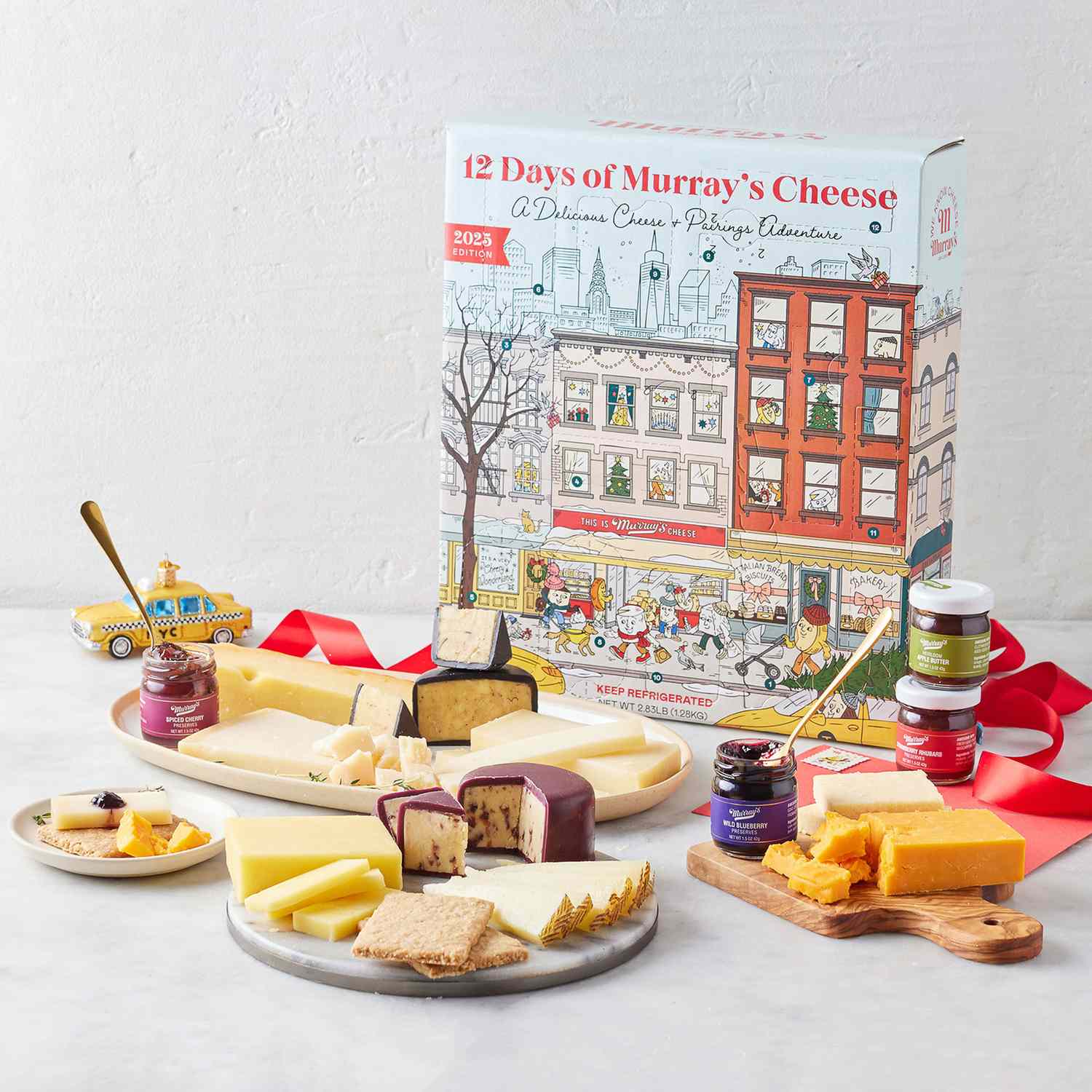 A holiday cheese board set with an assortment of cheeses and spreads displayed in front of a 12 Days of Murrays Cheese advent box