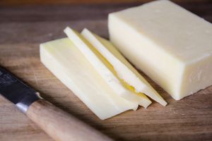 A block of cheese and several slices on a wooden surface with a knife beside them