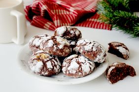 A plate of chocolate cookies with powdered sugar a red cloth and green foliage in the background