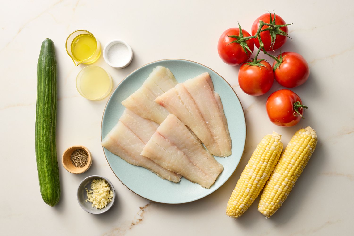 Arrangement of salad ingredients including fish fillets, tomatoes, cucumber, corn, and seasoning bowls