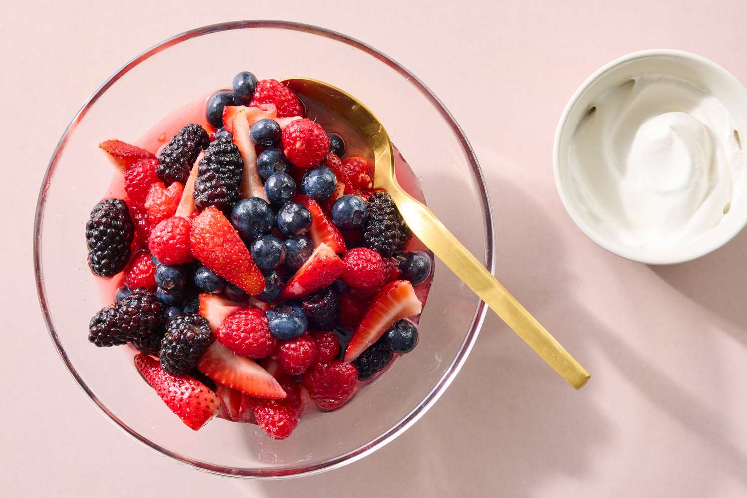 A bowl of mixed berries with a spoon accompanied by a side of cream in a small bowl