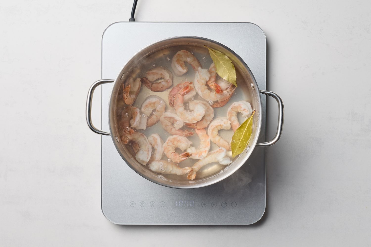 Shrimp cooking in a pot with bay leaves on a stovetop