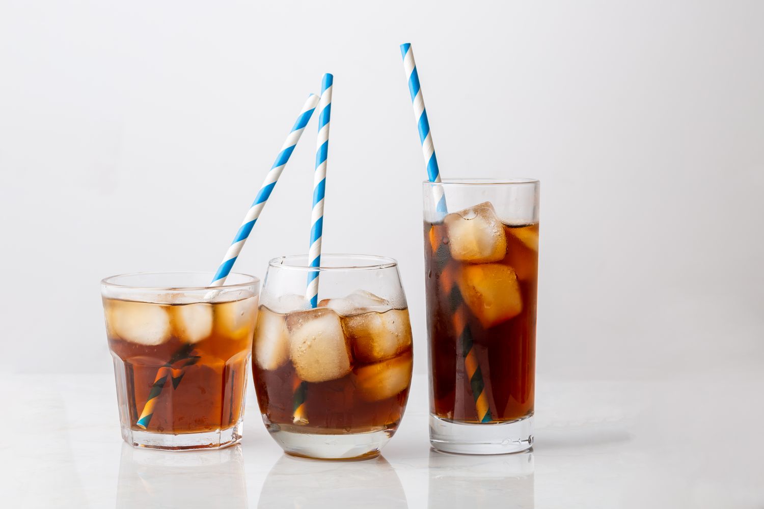 Three glasses of iced beverages with striped straws on a reflective surface