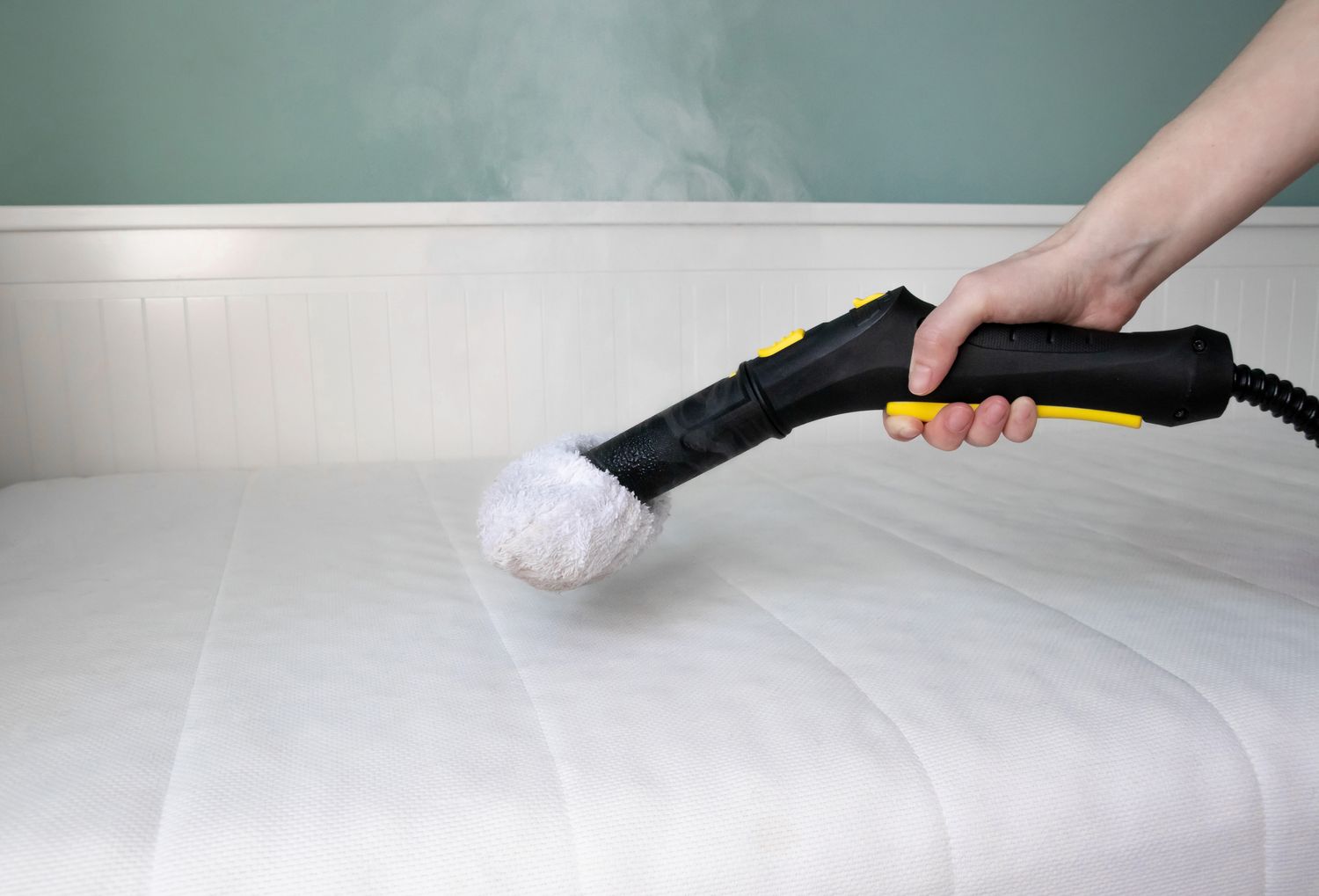 A handheld steam cleaner being used on a mattress