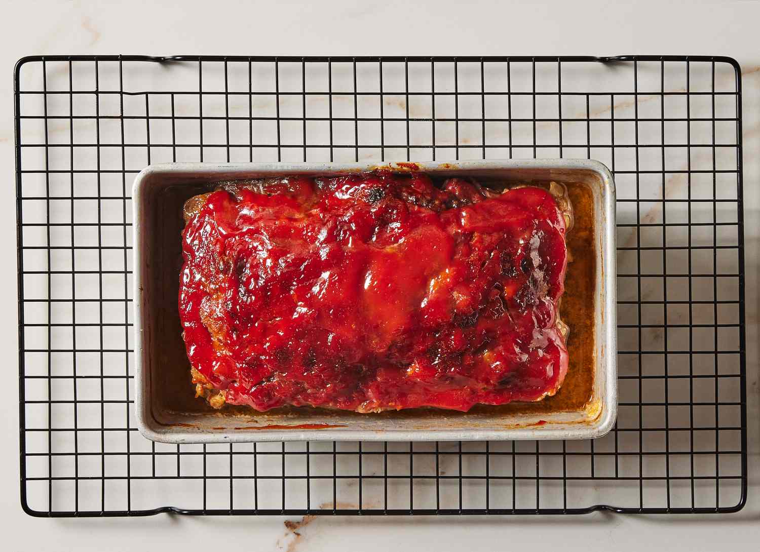 baked meatloaf in a pan resting on a cooling rack