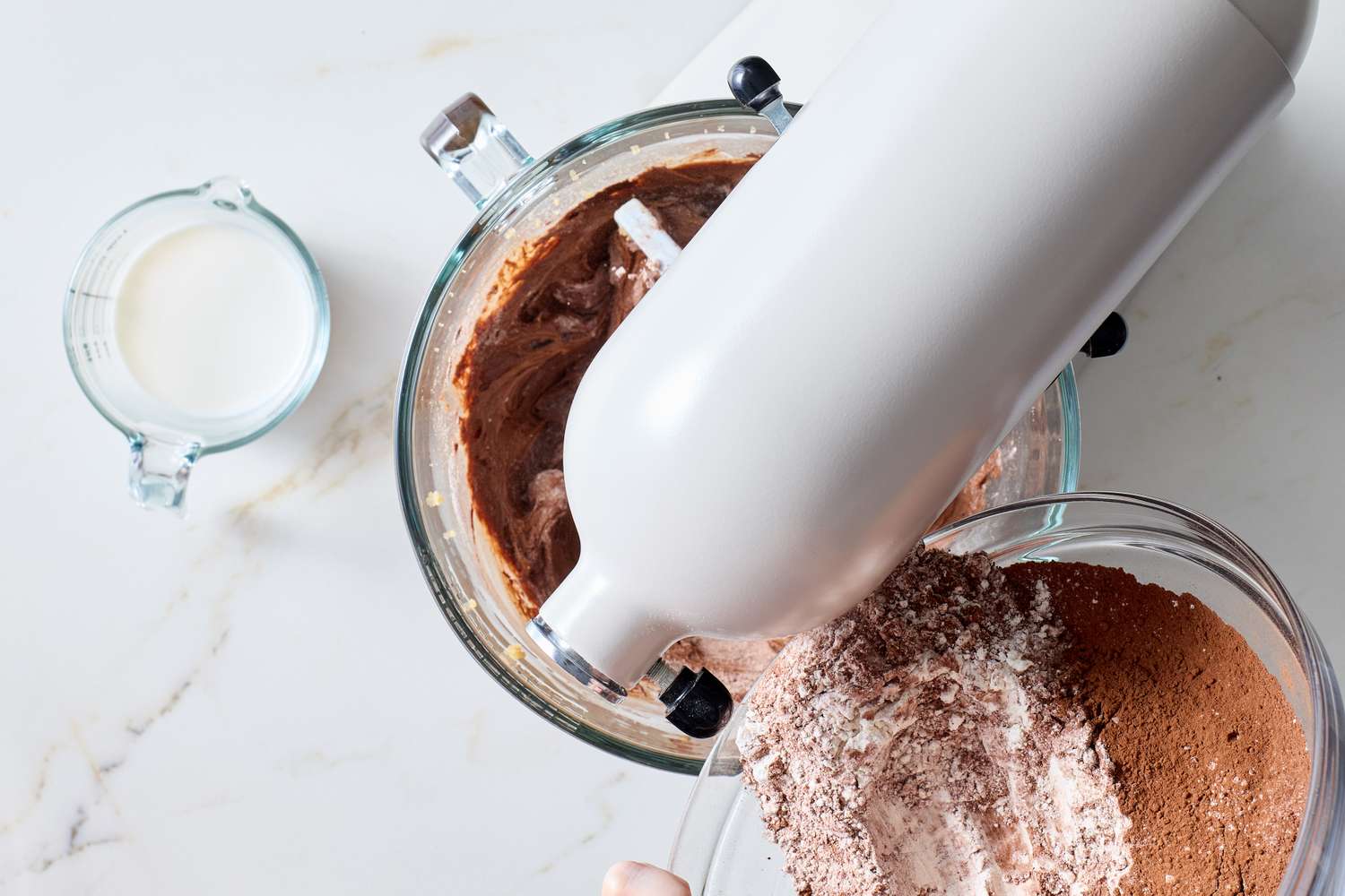 Mixing cocoa powder and flour into chocolate cookie batter with a stand mixer a measuring cup of milk nearby on the counter