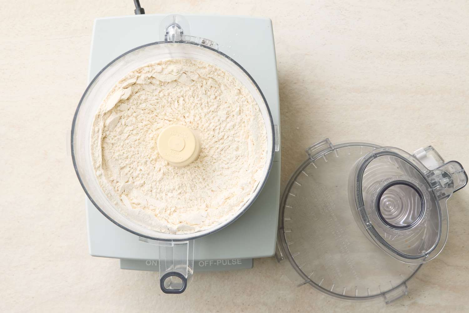 Food processor with dry ingredients being mixed for a recipe lid removed and placed to the side