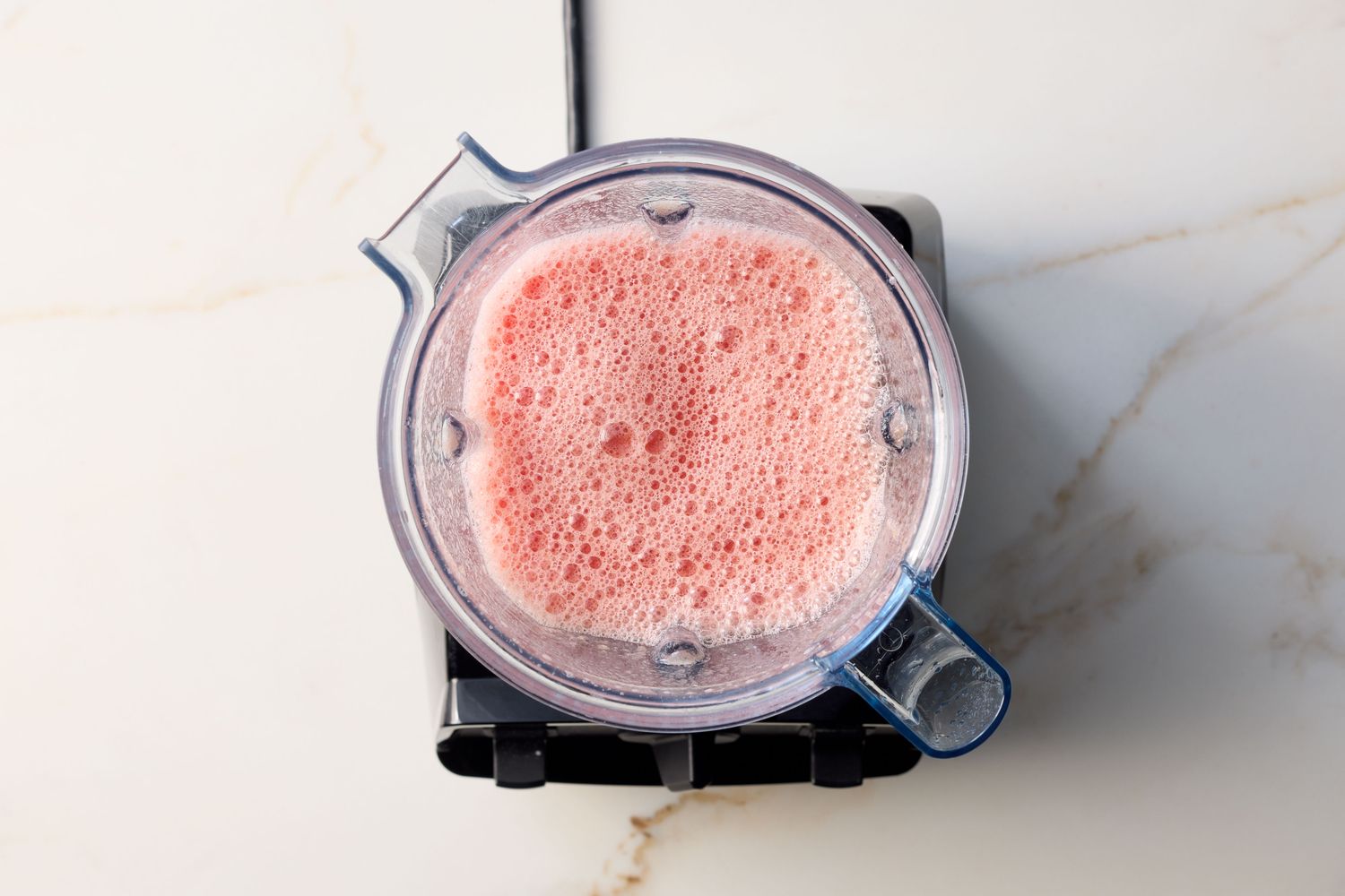 A blender containing frothy pink liquid on a counter