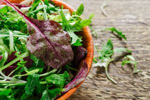 Mix of leaves of arugula, lettuce in a wooden bowl on a wooden table.