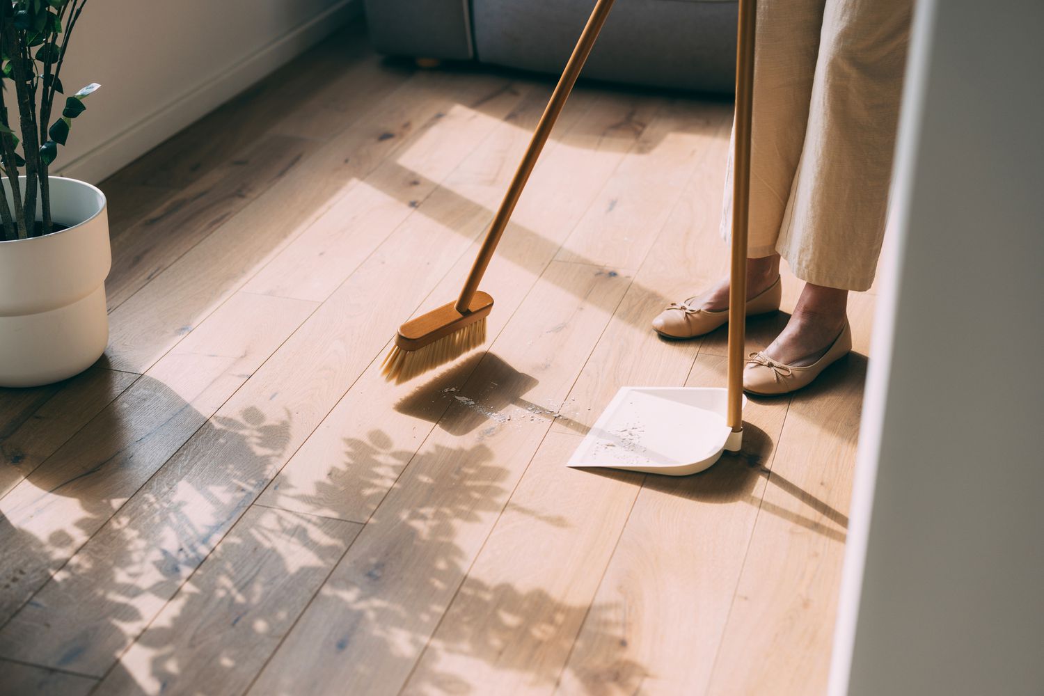 A person sweeping a wooden floor with a broom and dustpan