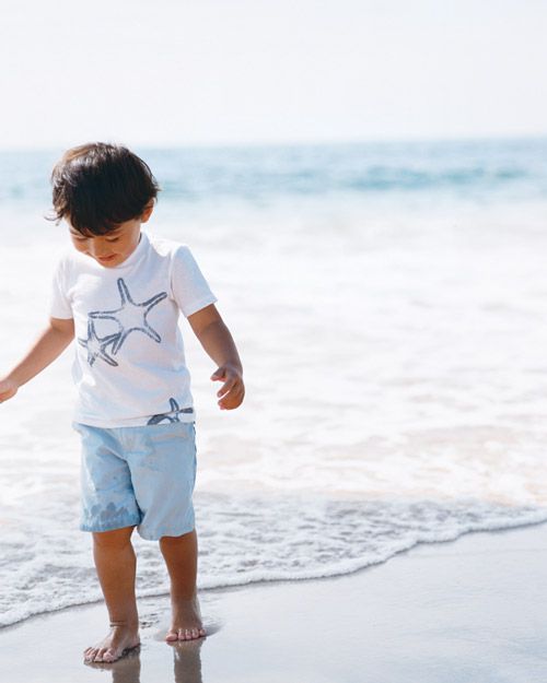 boy walking on beach wearing shell t-shirt