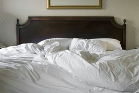 A bed with a wooden headboard and unmade white sheets and pillows in a room with partially visible decor