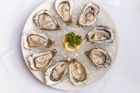 A plate of oysters on a bed of ice with a garnish of parsley and lemon slice in the center