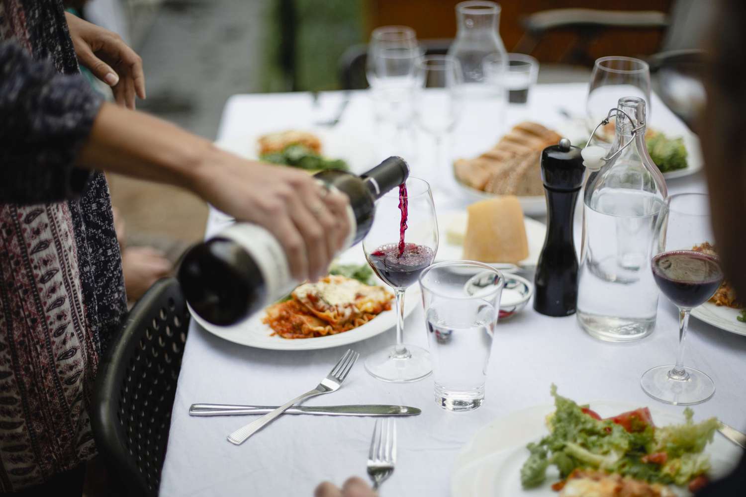 woman pouring red wine at dinner table