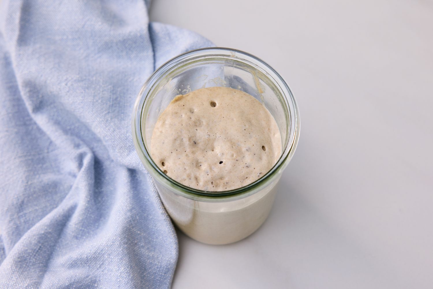 A jar containing sourdough starter placed on a surface next to a cloth