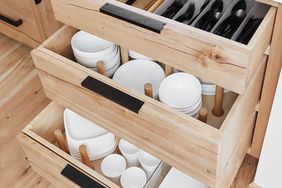 Open wooden kitchen drawers organized with plates bowls cups and utensils
