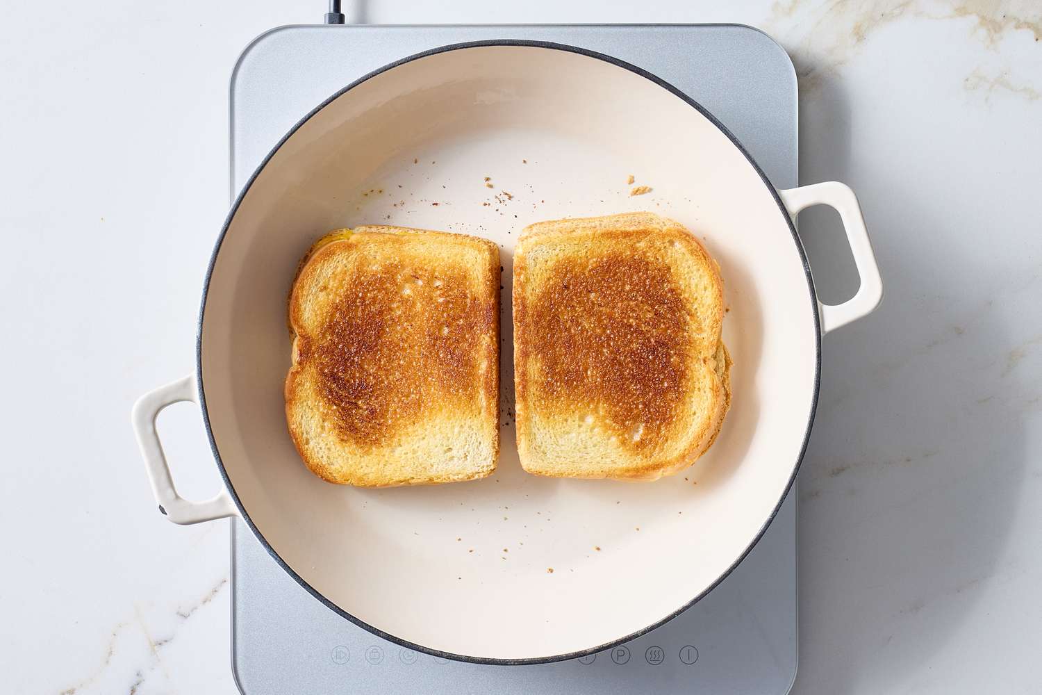 Two slices of grilled cheese being cooked in a white pan on a stovetop