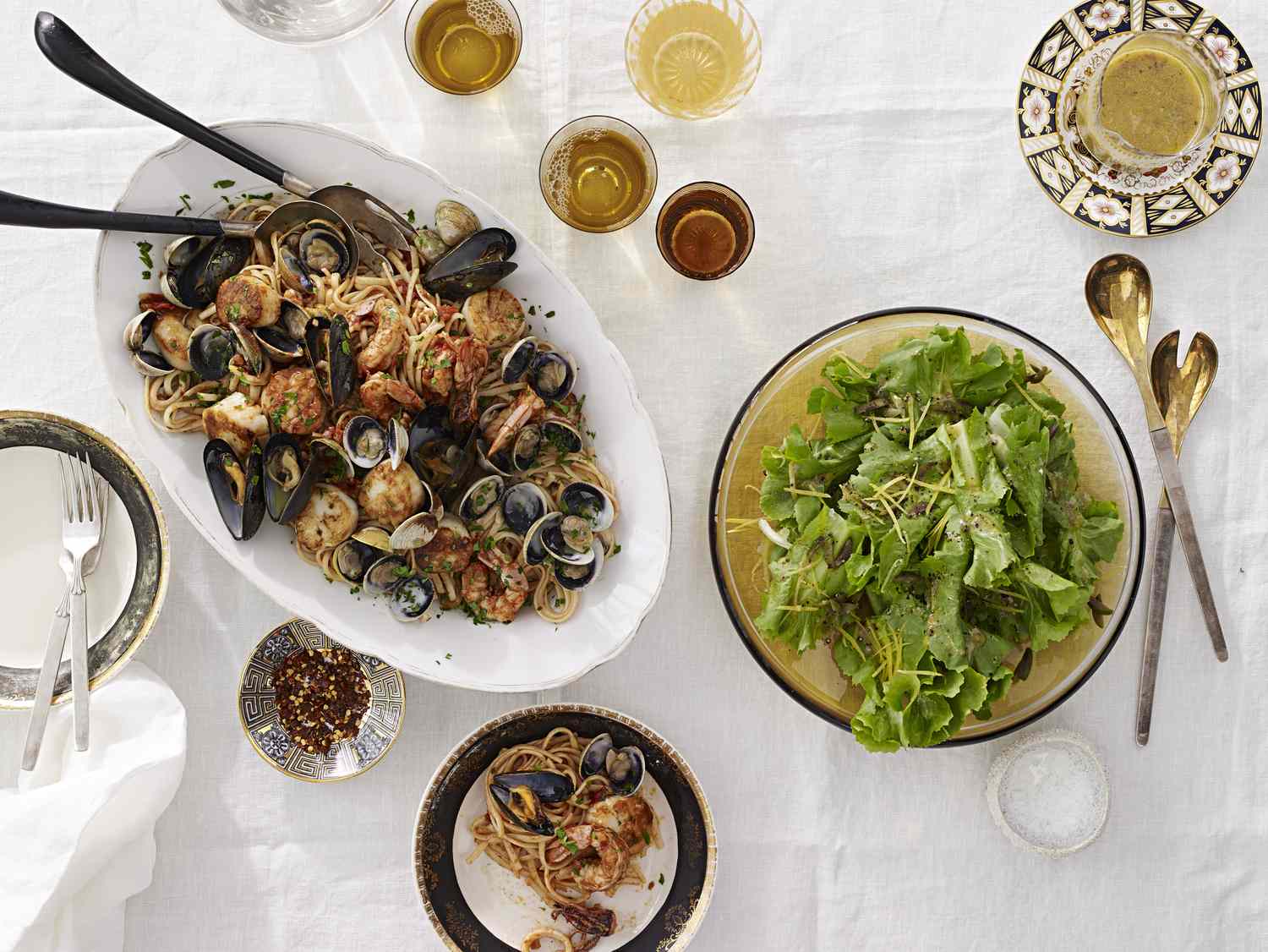 A meal on a table featuring seafood pasta a green salad and drinks