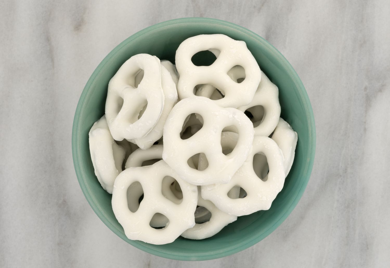 Top view of yogurt covered pretzels in a green bowl atop a gray marble cutting board.