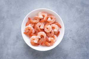 Cooked shrimp arranged in a white bowl on a gray surface