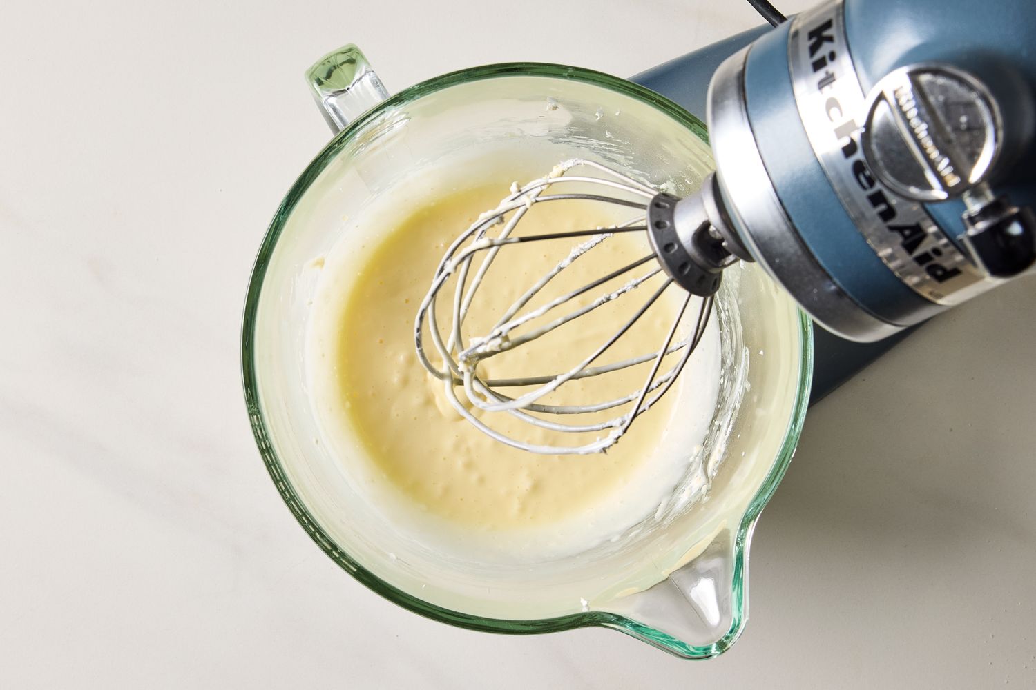 Mixer with whipped cheesecake batter in a glass bowl