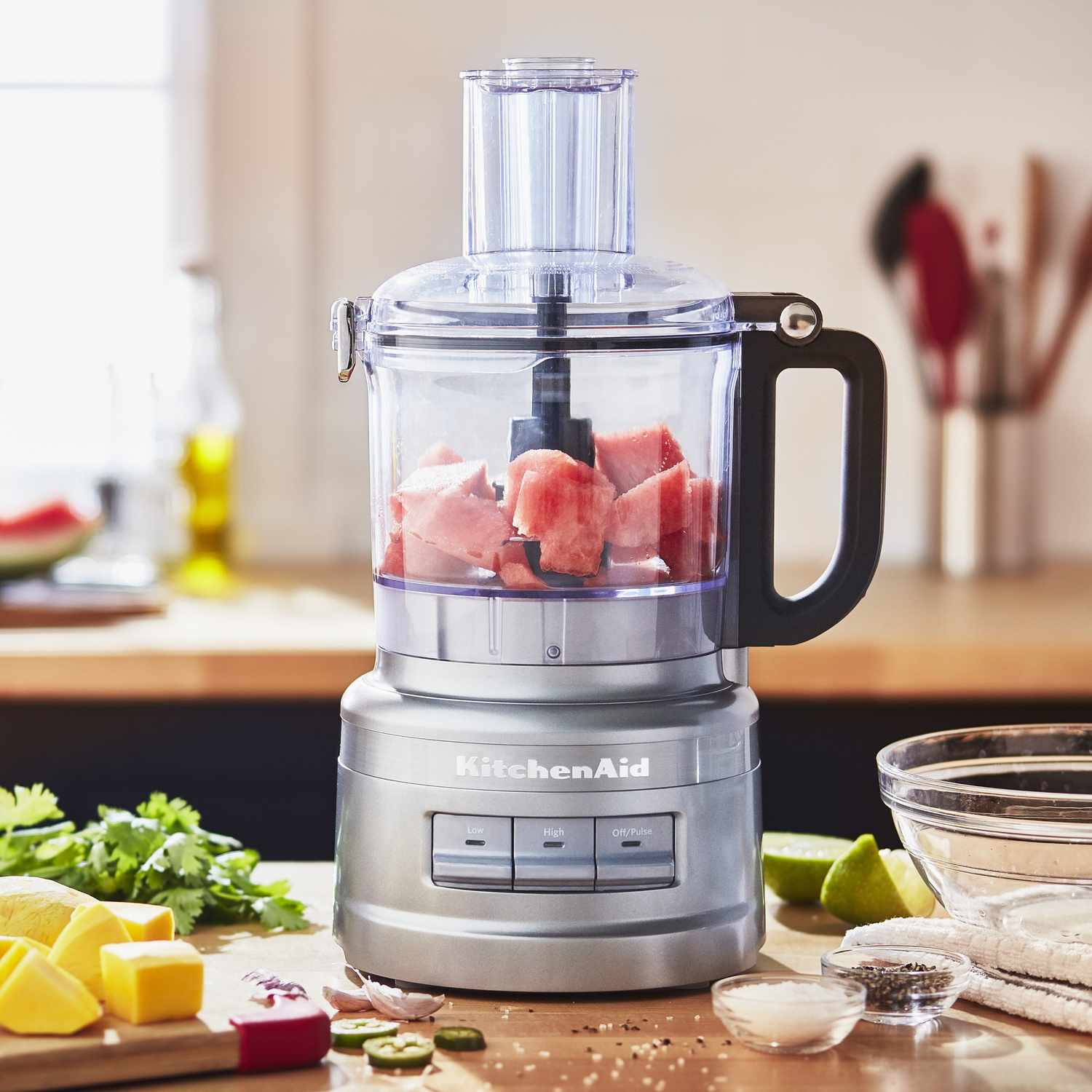 KitchenAid 7cup food processor with chopped ingredients inside placed on a kitchen countertop with various food items nearby