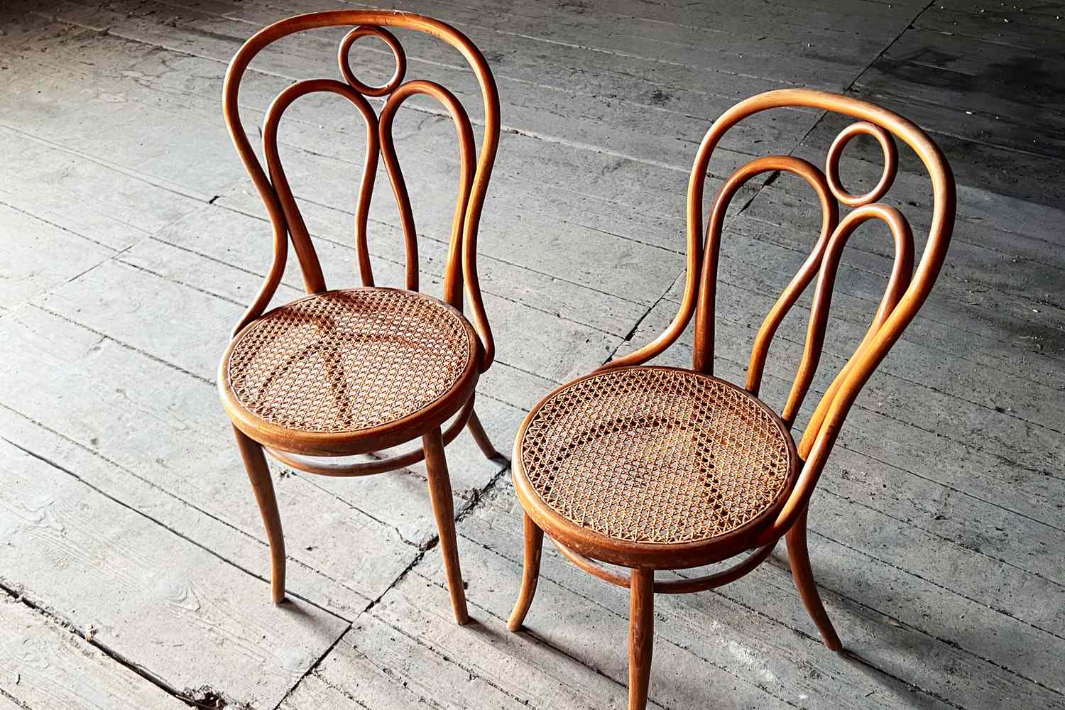 Two wooden chairs with curved backs and woven seats placed on a wooden floor