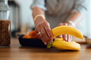 A person picking up bananas from a wooden table with other fruits visible in the background