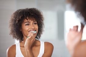woman looking in mirror brushing teeth