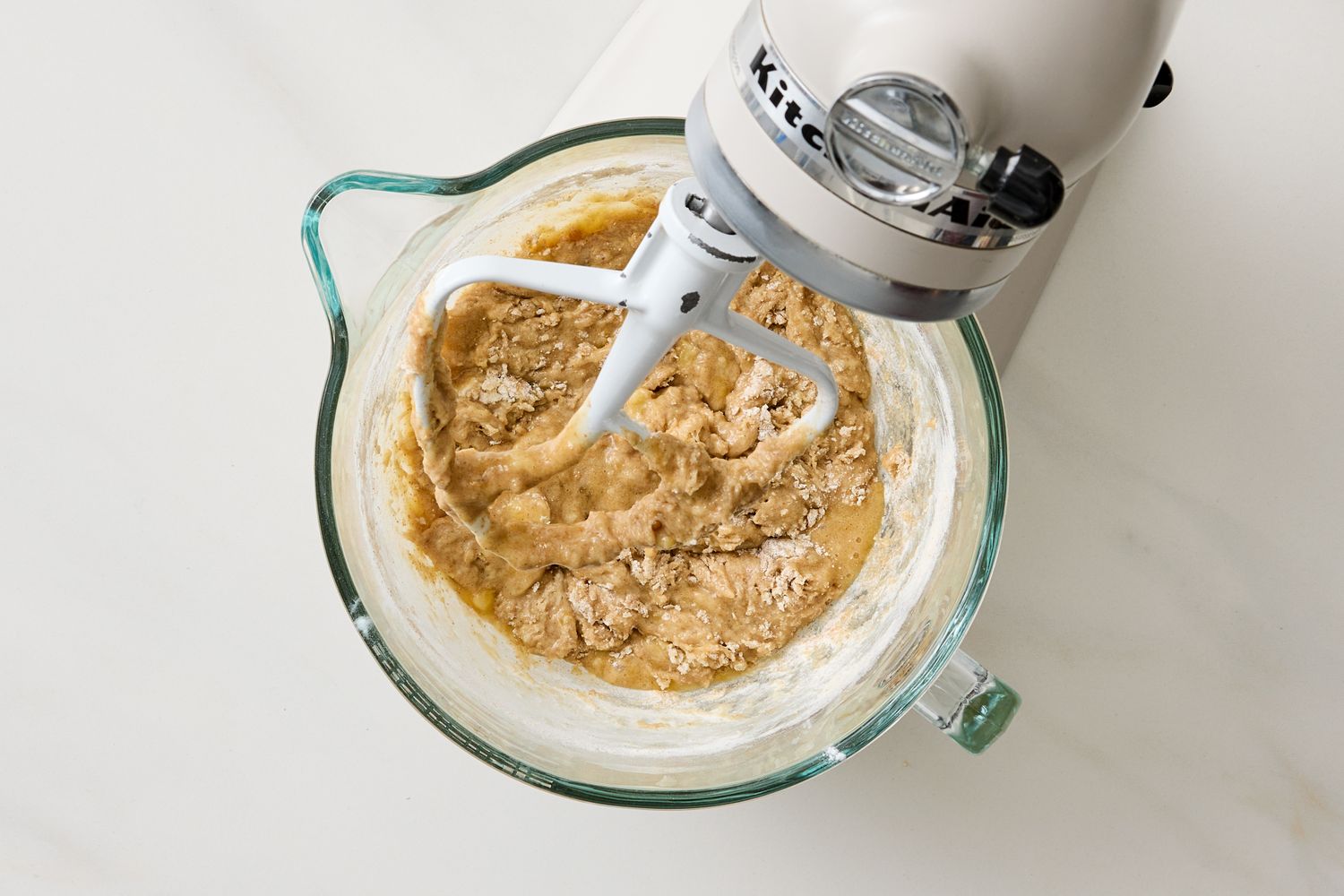 A mixing bowl and stand mixer with batter being prepared ingredients for banana muffins