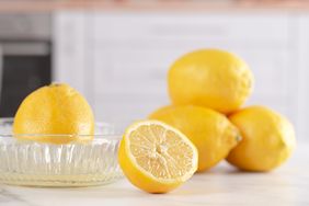 lemon being juiced in glass manual juicer and more lemons on marble counter
