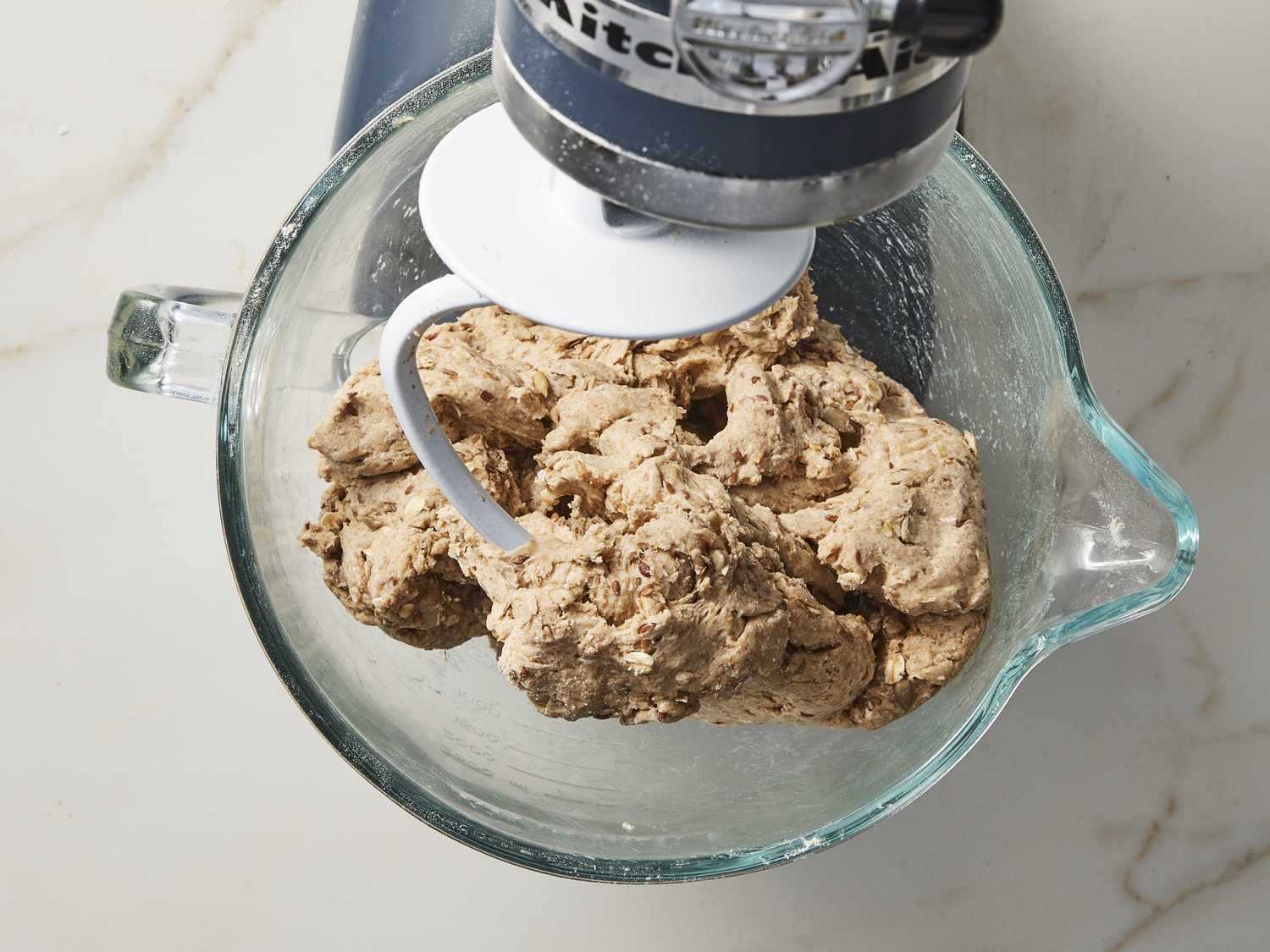 Multigrain bread dough in glass bowl under stand mixer