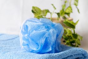 A loofah on a folded towel with green leaves in the background