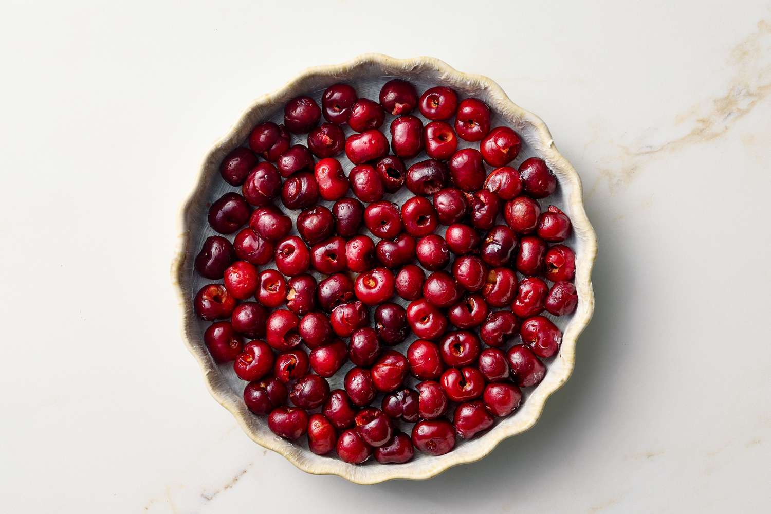 A shallow dish filled with whole cherries, prepared for a recipe or dessert