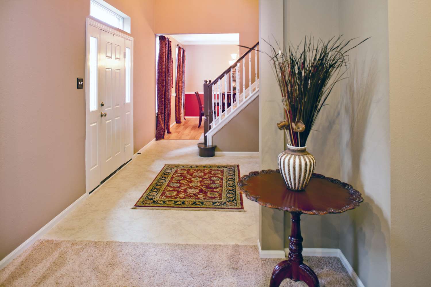 A home interior featuring an entryway with a table and vase stairs leading up and a view into a dining area