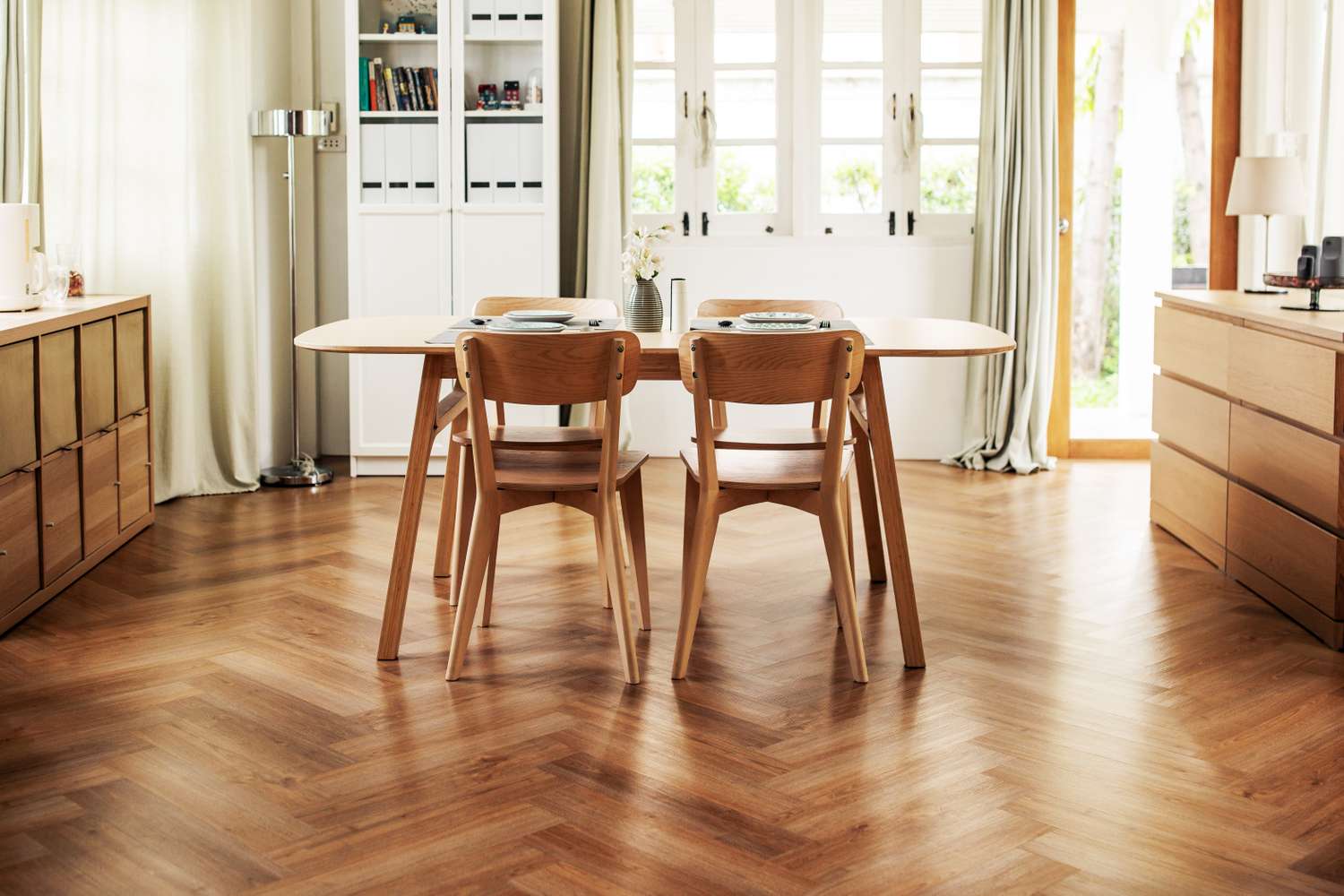A dining area with a wooden floor a round table set with dishes and wooden chairs under natural light from nearby windows