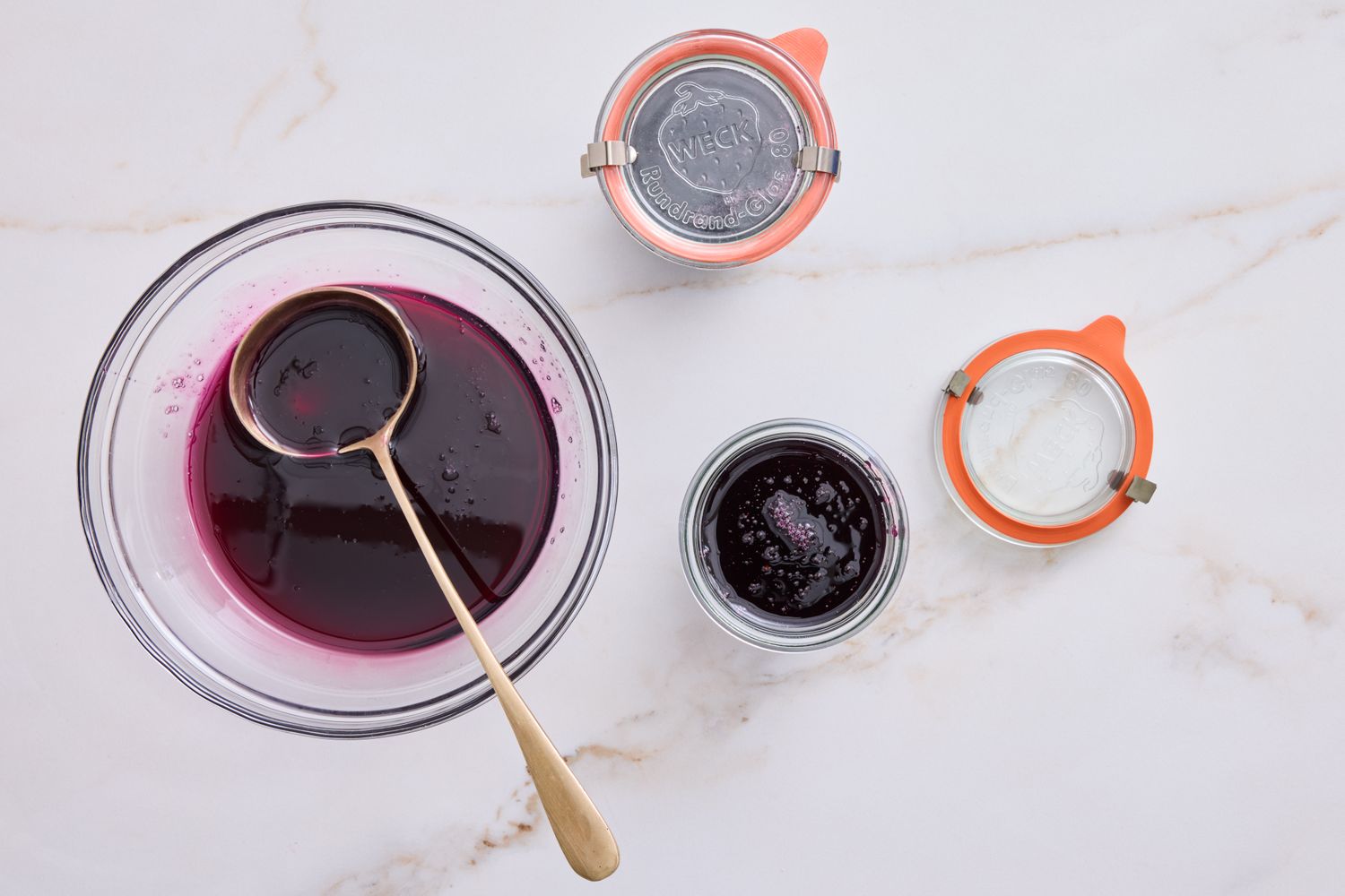 A bowl with jelly and a ladle next to two jars one filled and one empty