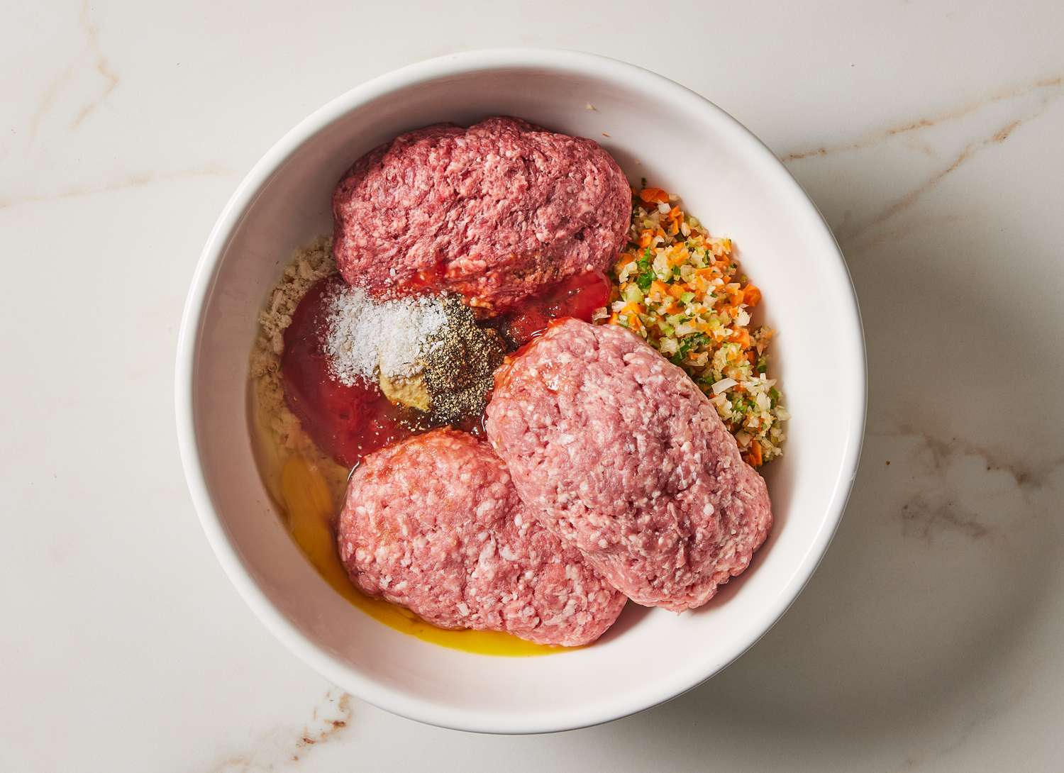 raw ground meat, vegetables and spices in a white bowl