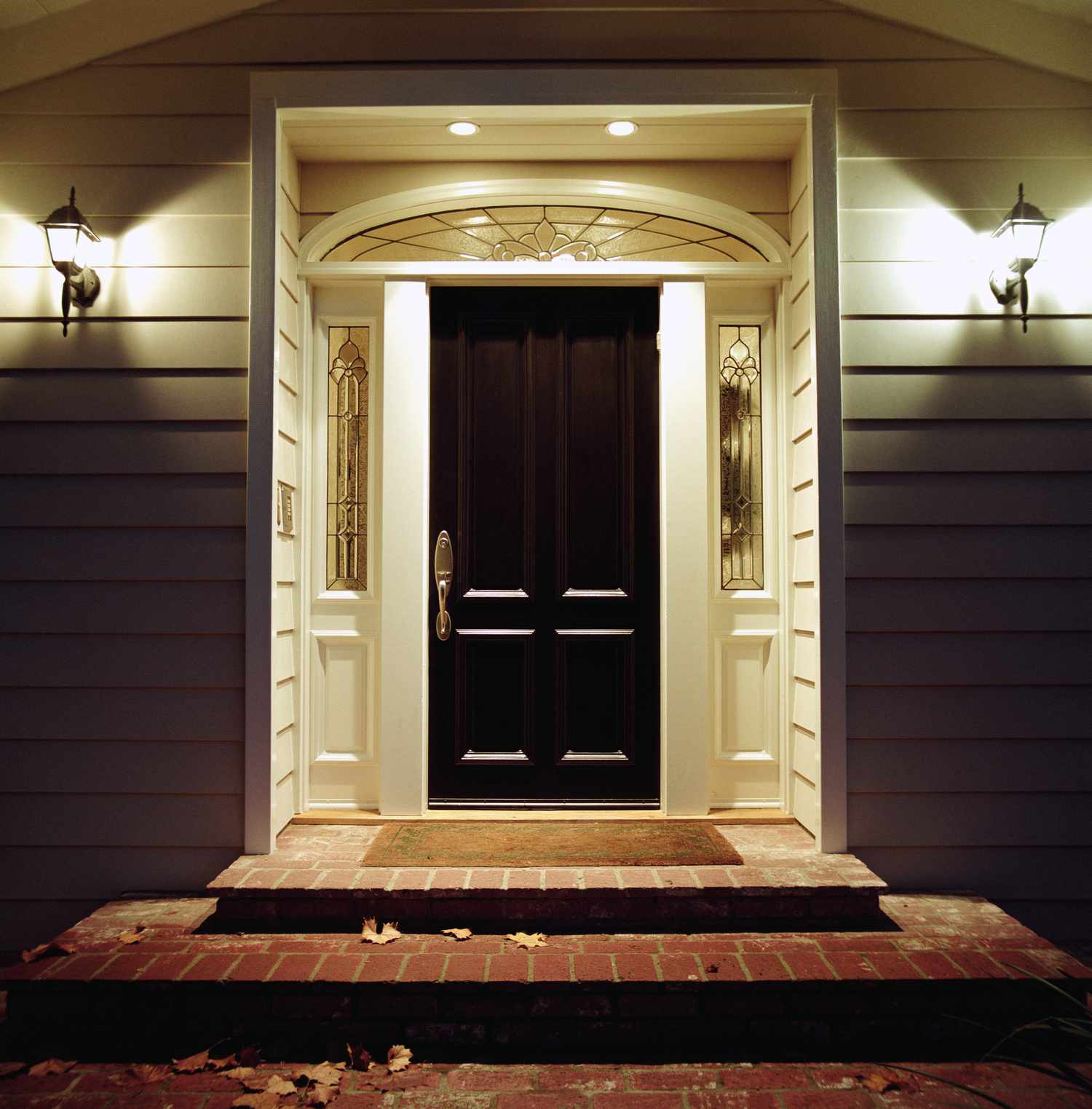 A front door of a house with steps leading to it symmetrically lit by wallmounted lanterns