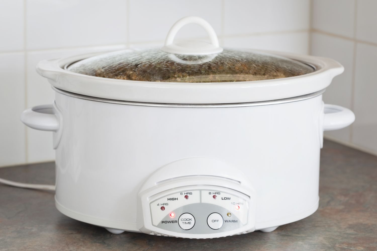 A slow cooker on a kitchen counter with the dial and settings visible