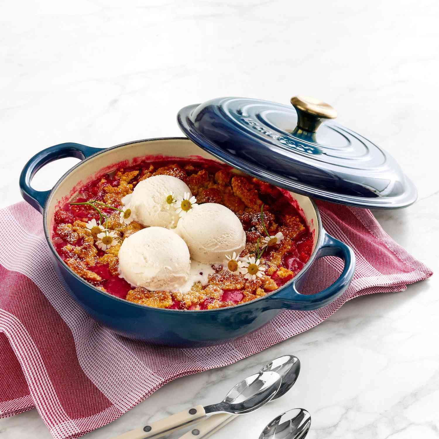 A Le Creuset cast-iron French oven containing dessert topped with scoops of ice cream, with its lid offset