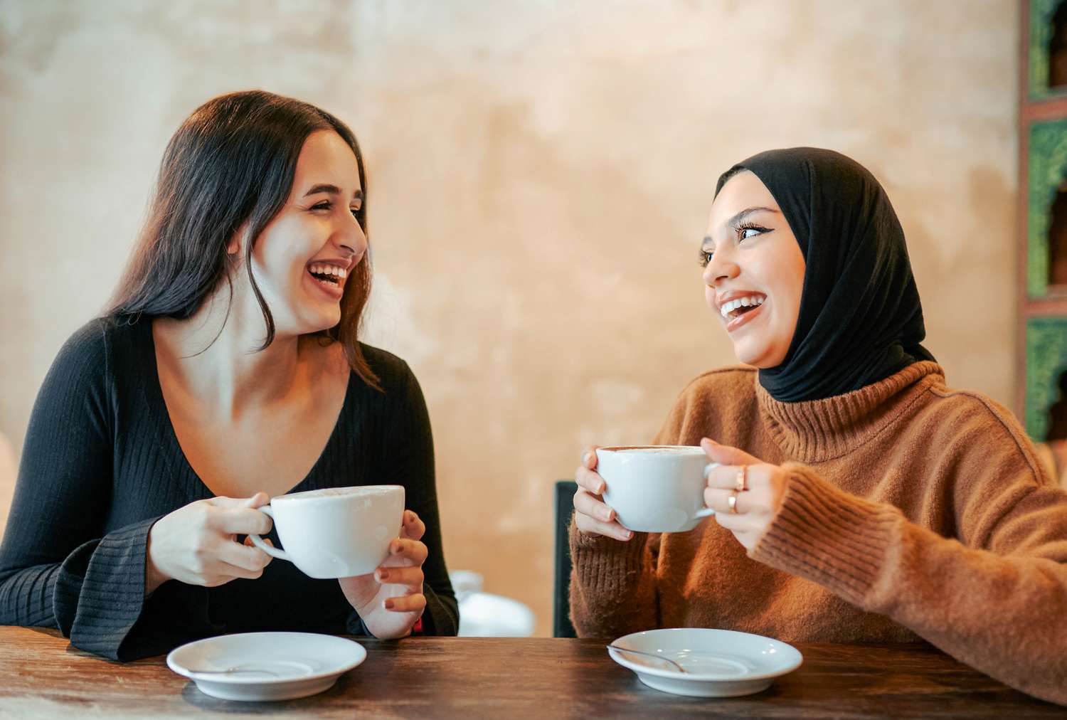 Two women sitting at a table holding cups smiling and conversing with each other