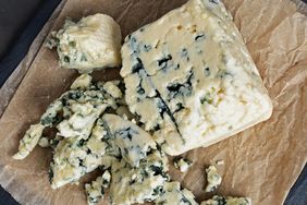 A block of blue cheese on parchment paper with crumbled pieces surrounding it
