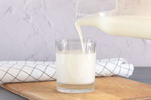 A glass of milk on a wooden surface being poured from a pitcher