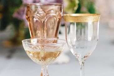Various glasses arranged on a table including a wine glass with gold trim and a coupe glass with liquid