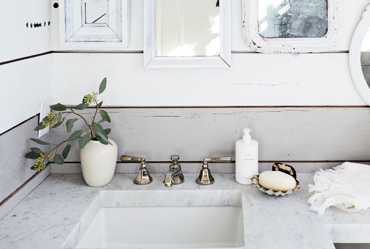 Bathroom vanity with a marble countertop a small vase holding greenery a soap dispenser a soap dish and a folded towel